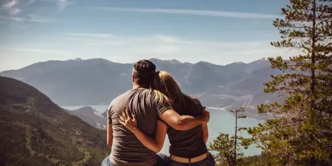 Un couple partage un moment d'amour sensuel, bras dessus, bras dessous, contemplant un paysage montagneux et un lac paisible.