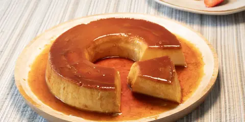 Un delicioso flan de leche condensada con caramelo líquido, servido en un plato de madera.
