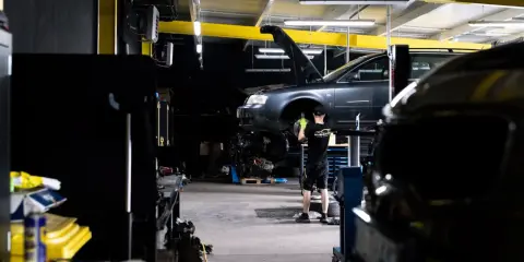 Mechanik bada przyczynę, dlaczego auto nie odpala. Podniesiony przód pojazdu i widoczny silnik sugerują skomplikowaną usterkę.