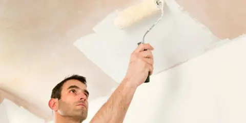 Hombre pintando el techo con rodillo. Se ve la mano sujetando el rodillo y la pintura blanca aplicándose.