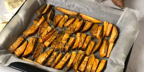 Patate dolci al forno tagliate a spicchi, condite con rosmarino e spezie, pronte per essere gustate.