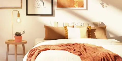 Acogedora habitación con decoración nórdica, cama con mantas y cojines cálidos, mesita de noche con planta y lámpara, y cuadros en la pared.