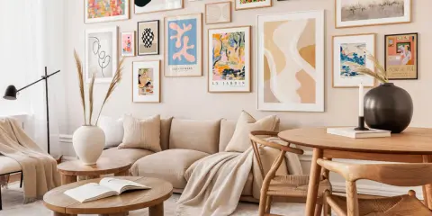 Un salón moderno con un sofá beige y una colección de cuadros para encima del sofá, llenos de color y formas abstractas.