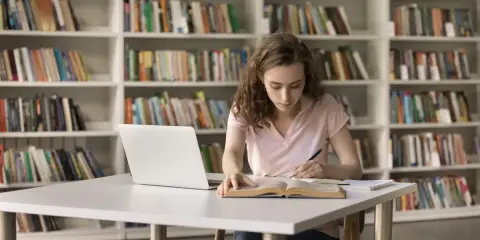 Młoda kobieta uczy się w bibliotece, zastanawiając się, czy studia chemiczne to dobry wybór.