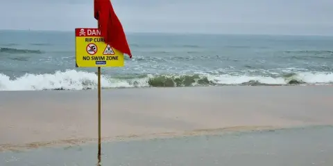 Röd flagga och skylt varnar för farliga strömmar vid stranden i Goa, Indien. Ingen badzon.