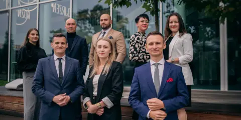 Grupa prawników w eleganckich strojach pozuje przed budynkiem.