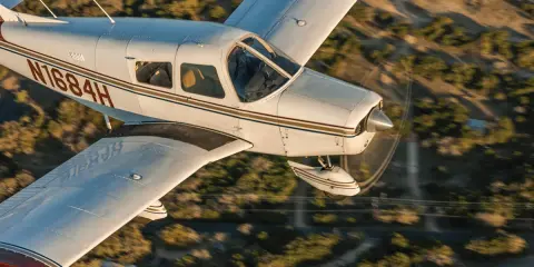 Eine Piper Cherokee 140 fliegt über eine bewaldete Landschaft.