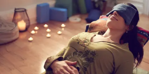 Kvinna med ögonbindel vilar under brahma yoga, omgiven av levande ljus och yogablock.