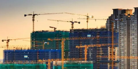 Grúas de construcción trabajando en la edificación de rascacielos, mostrando los elementos estructurales de un edificio en proceso.