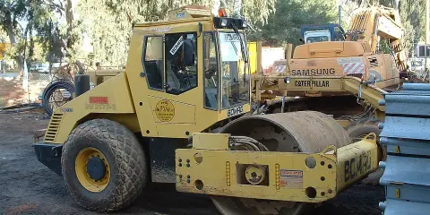 Żółty walec drogowy BOMAG BW 213D-3 na placu budowy, obok koparki Samsung Caterpillar.