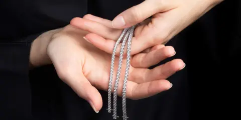 Mani delicate tengono tre scintillanti bracciali tennis, un classico intramontabile la cui storia affonda le radici nel mondo dello sport.