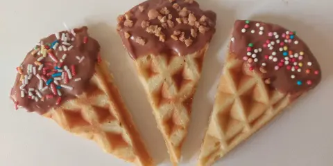 Drei dreieckige Waffeln, mit Schokolade überzogen und bunt bestreut, warten darauf, von Kindern beim Waffeln dekorieren vernascht zu werden.