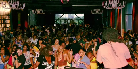 A vibrant crowd dances at a lively event, possibly one of the best gay bars in Chicago, under a disco ball and ornate chandeliers.