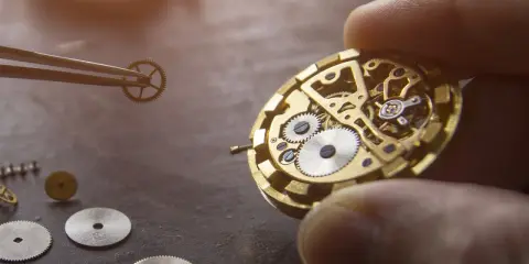 Un orologiaio assembla i componenti di un orologio meccanico, mostrando ingranaggi e molle dorate.