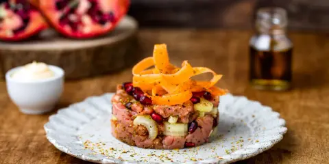 Deliziosa tartare di manzo con melograno, cipolla e carote a spirale, servita su un piatto rustico.