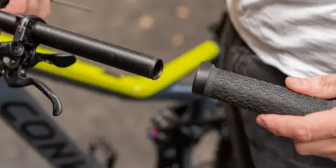 Person wechselt Fahrradgriffe. Der Lenker ist freigelegt, die neue Griff wird bereitgehalten.