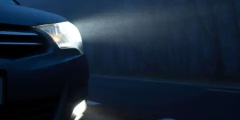 El alumbrado de posición de un coche ilumina la niebla en una carretera oscura.