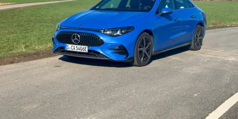 Blauer Mercedes-Benz CLA 250+ EQ auf einer Straße, mit grünen Feldern und einem Strommast im Hintergrund.