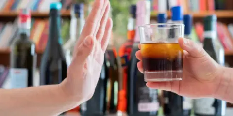 Dłoń odrzuca szklankę z alkoholem, symbolizując początek leczenia alkoholizmu.