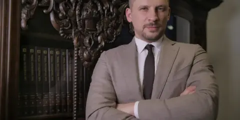 Mężczyzna w garniturze stoi na tle regału z książkami.