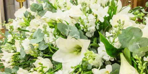 Piękna, biała wiązanka kwiatów z liliami, różami i zielonymi liśćmi.