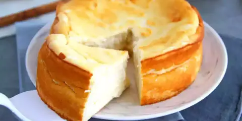 Le meilleur gâteau au fromage blanc, aérien et doré, est servi sur une assiette blanche. Une part est déjà coupée.