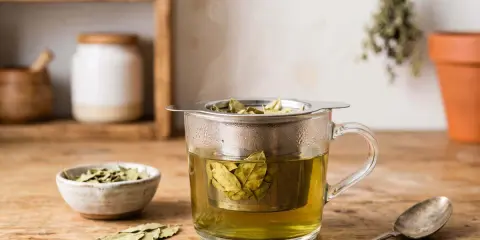 Infusion de feuille de séné, danger potentiel pour la santé. Une tasse de thé fumant avec des feuilles dans un infuseur, à côté d'un bol de feuilles séchées et d'une cuillère.