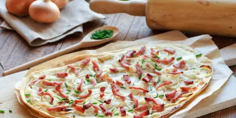Flammekueche prête à être dégustée, avec ses oignons, lardons et ciboulette. Une recette facile pour un repas convivial.