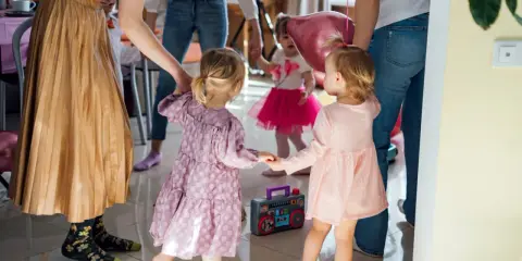 Radosne zabawy taneczne dla dzieci! Maluchy w kolorowych sukienkach trzymają się za ręce, tańcząc przy grającym radiu.