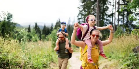 Rodzina wędruje po górach, dzieci siedzą na karkach rodziców. Wspaniały długi weekend sierpnia w otoczeniu natury.