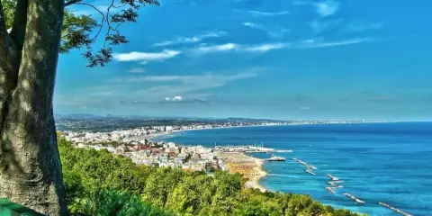 Vista panoramica della Riviera Romagnola con mare azzurro, spiagge affollate e una città costiera. Ideale per il turismo.