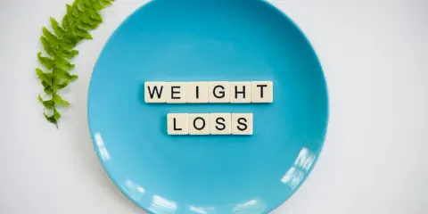 Niebieski talerz z literami tworzącymi napis "WEIGHT LOSS" i gałązką paproci. Pytanie o makro na redukcji?