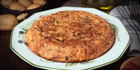 Tortilla española, un clásico de la comida típica de Granada, servida en un plato decorado. Patatas y aceite en el fondo.