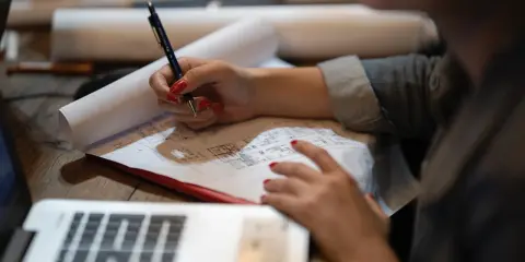Rysunek techniczny, przypominający wyrys z rejestru gruntów, na którym osoba z czerwonymi paznokciami pisze długopisem.