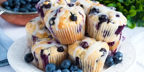 Stosik pysznych muffinek z borówkami, polanych lukrem, ozdobiony świeżymi owocami.