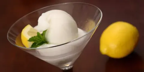 Glace colonel rafraîchissante dans un verre à martini, garnie d'une tranche de citron et de menthe. Un citron entier est posé à côté.