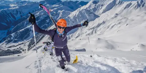 Ein Mann im orangefarbenen Helm jubelt beim Skyrunning in den verschneiten Alpen.