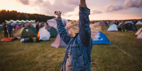 Ragazza con le braccia alzate in un campo di tende, immersa nell'atmosfera di uno dei festival techno più famosi.
