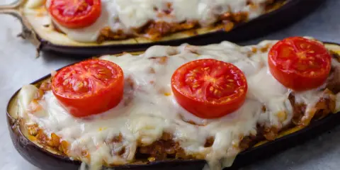 Deux aubergines farcies, garnies de tomates et de fromage fondu, prêtes à être dégustées.