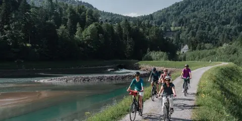 Gruppe genießt MTB Touren entlang eines Flusses mit bewaldeten Hügeln im Hintergrund.