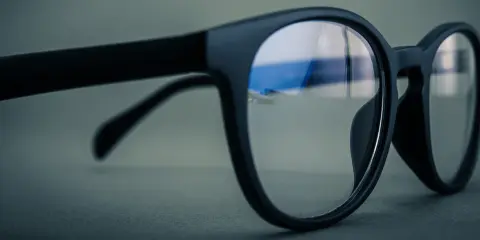 Okulary z czarnymi oprawkami, soczewki z niebieskim antyrefleksem odbijają światło.
