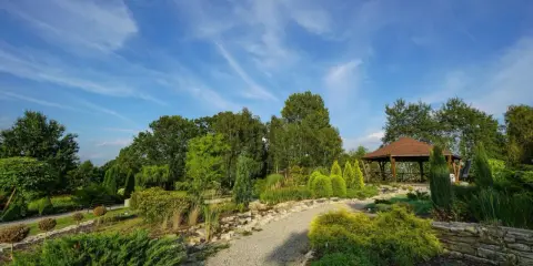 Malownicze ogrody botaniczne na Śląsku z altaną i kamiennymi ścieżkami, otoczone bujną zielenią pod błękitnym niebem.