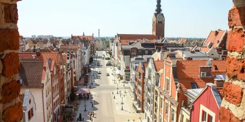 Widok z góry na urokliwą elbląg starówkę z kolorowymi kamieniczkami i wieżą kościelną w tle.