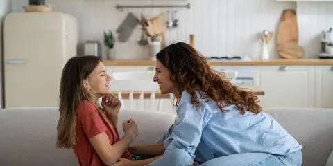 Madre e hija ríen en el sofá. Ella le enseña como es la primera regla de una niña: la empatía.