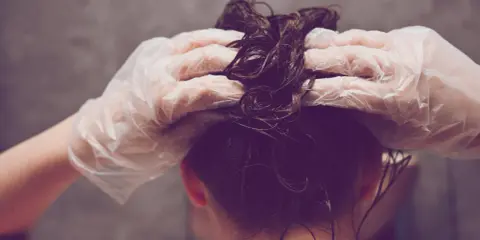 Hände mit Handschuhen tragen Olaplex Nr. 3 auf nasses, dunkles Haar auf.