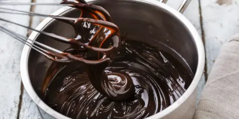 Fouet mélangeant du chocolat noir brillant dans une casserole, étape clé pour le tempérage.