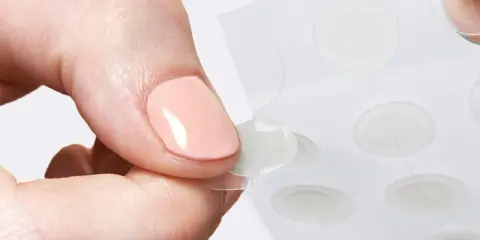 Une main retire délicatement un patch boutons d'une feuille, prêt à agir contre les imperfections.