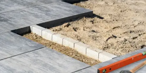 Budowa tarasu z bloczków betonowych w piasku. Poziomica i młotek czekają na dalsze prace.