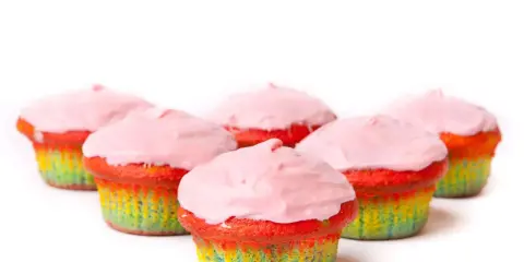 Bunte Muffins mit Lebensmittelfarbe und rosa Zuckerguss, die wie ein Regenbogen aussehen.