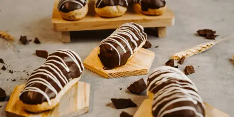 Éclairs gourmands avec un glaçage éclair chocolat brillant, décorés de fines rayures blanches. Des éclats de chocolat parsèment la table.